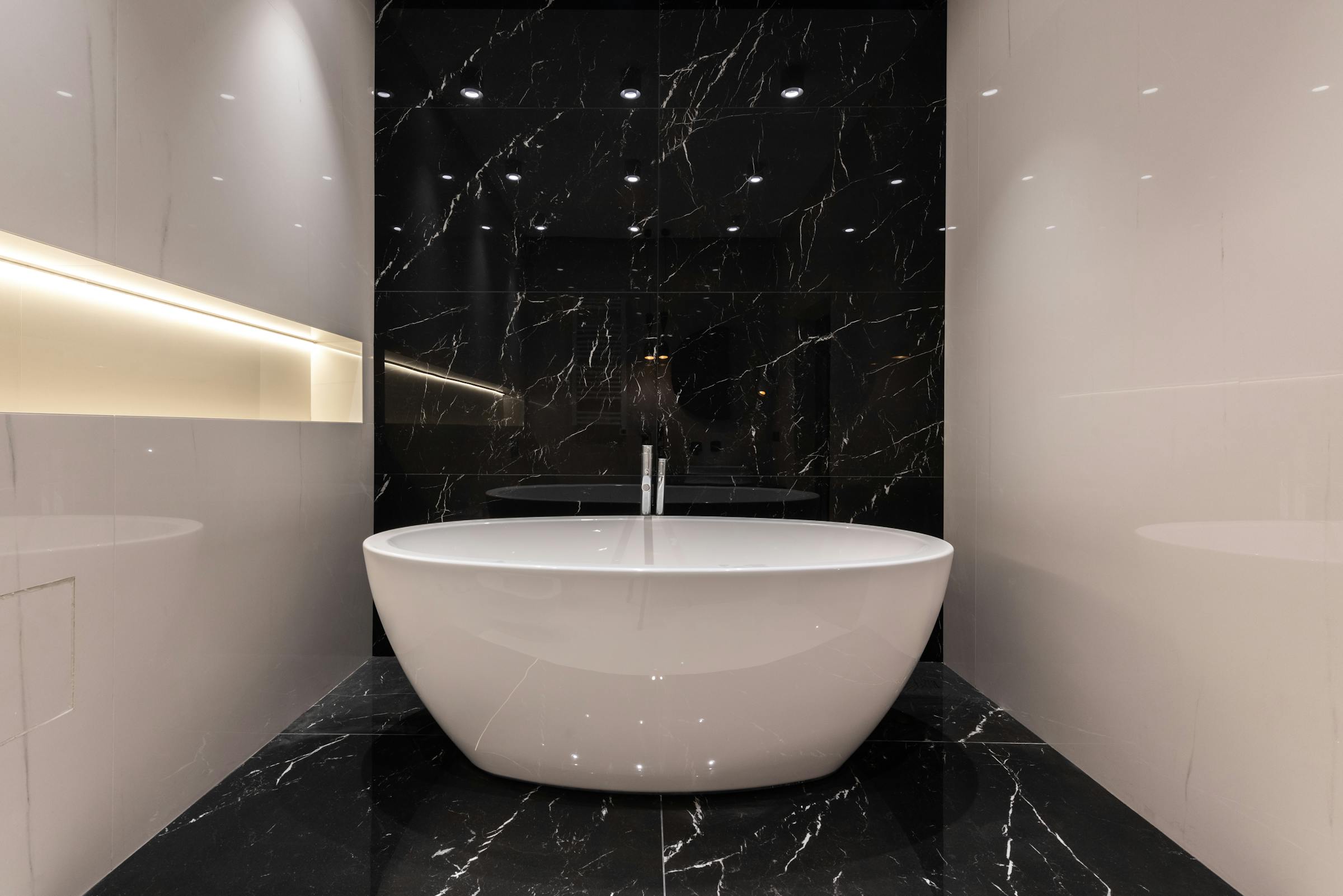 Freestanding tub against a black marble feature wall